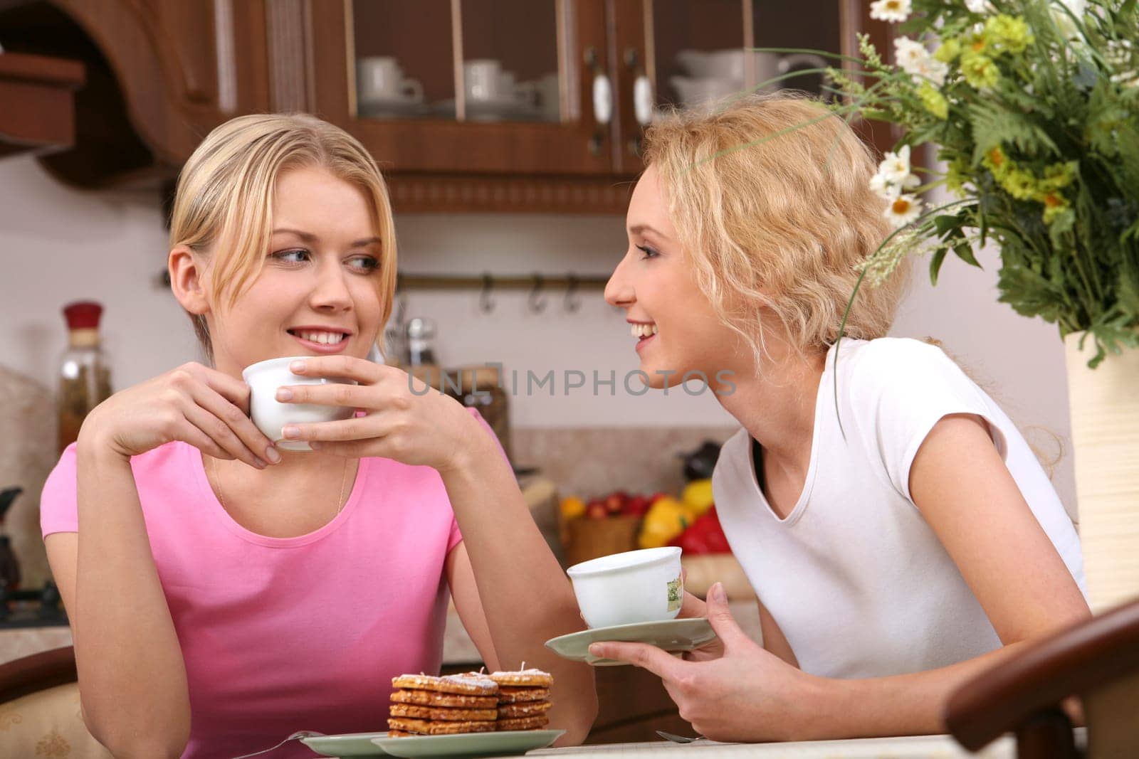 Two smiling girls have tea with tasty cookies in the kitchen