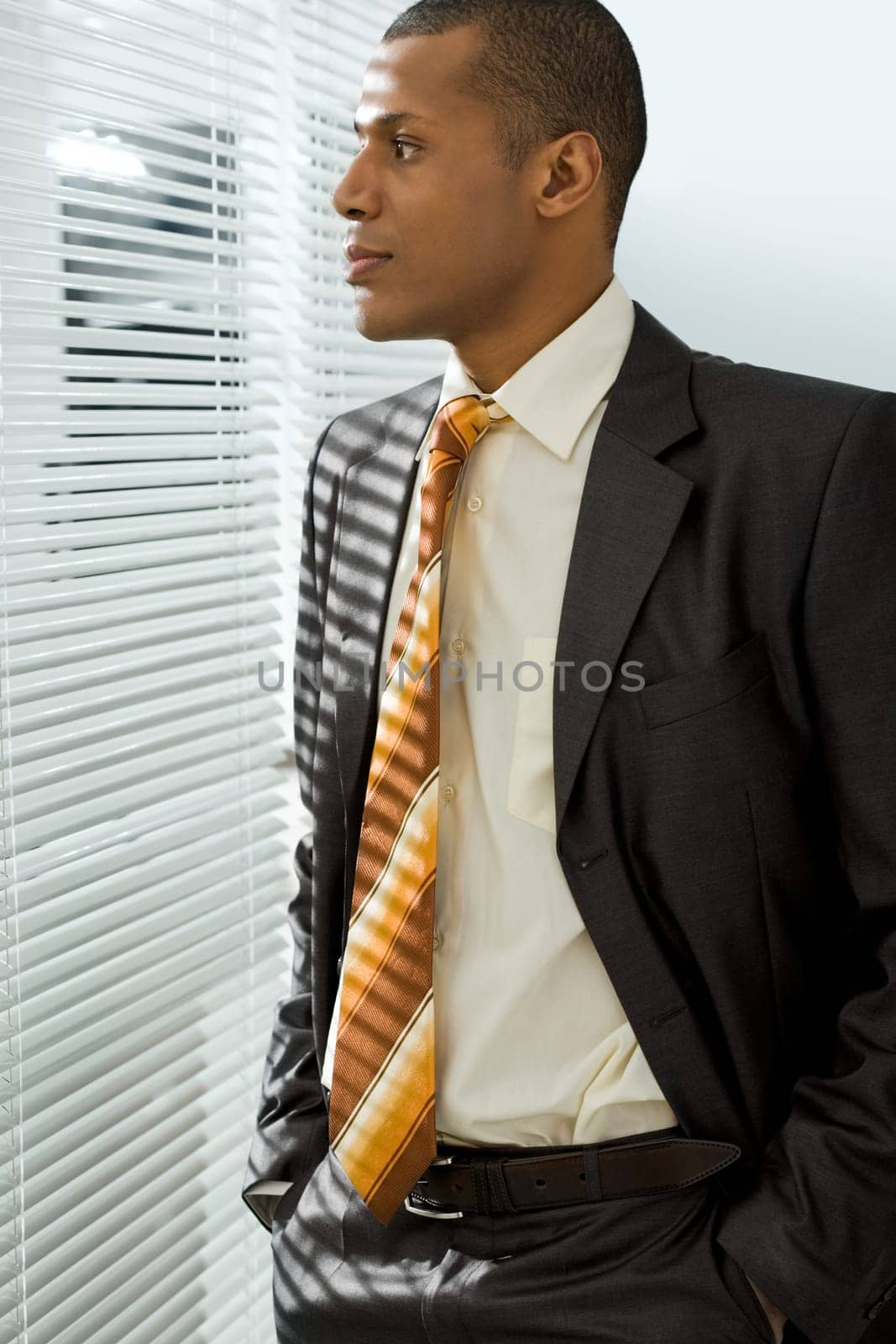 Serious businessman standing and looking through venetian blind in office