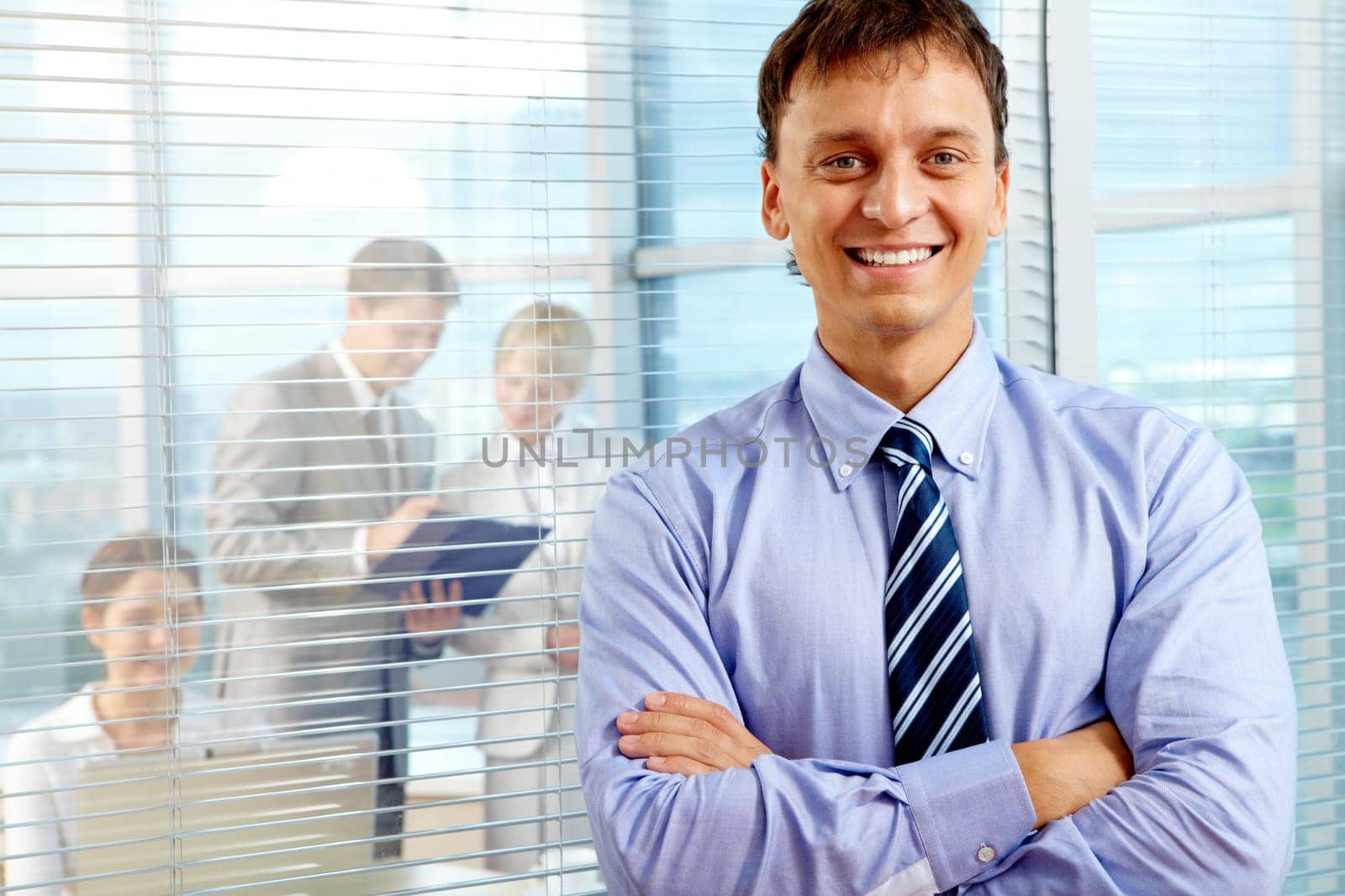 Business leader looking at camera with team of partners working in office behind