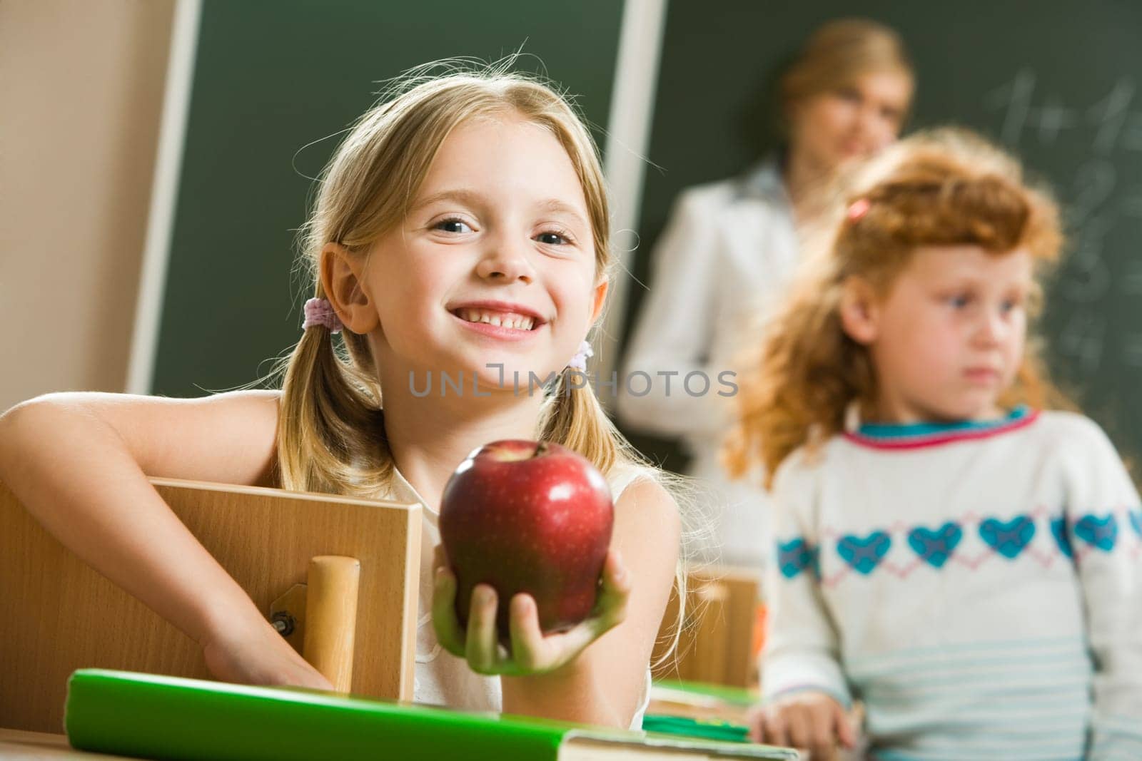 Portrait of happy pretty girl holding a red apple in the classroom