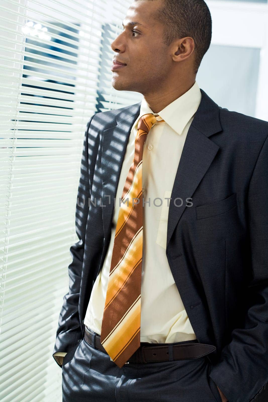 Serious businessman standing and looking through venetian blind in office