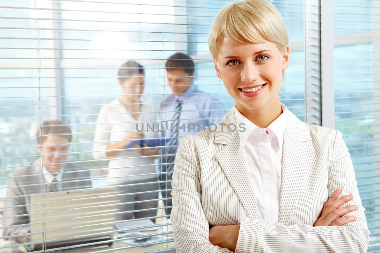Female leader looking at camera with team of partners working in office behind