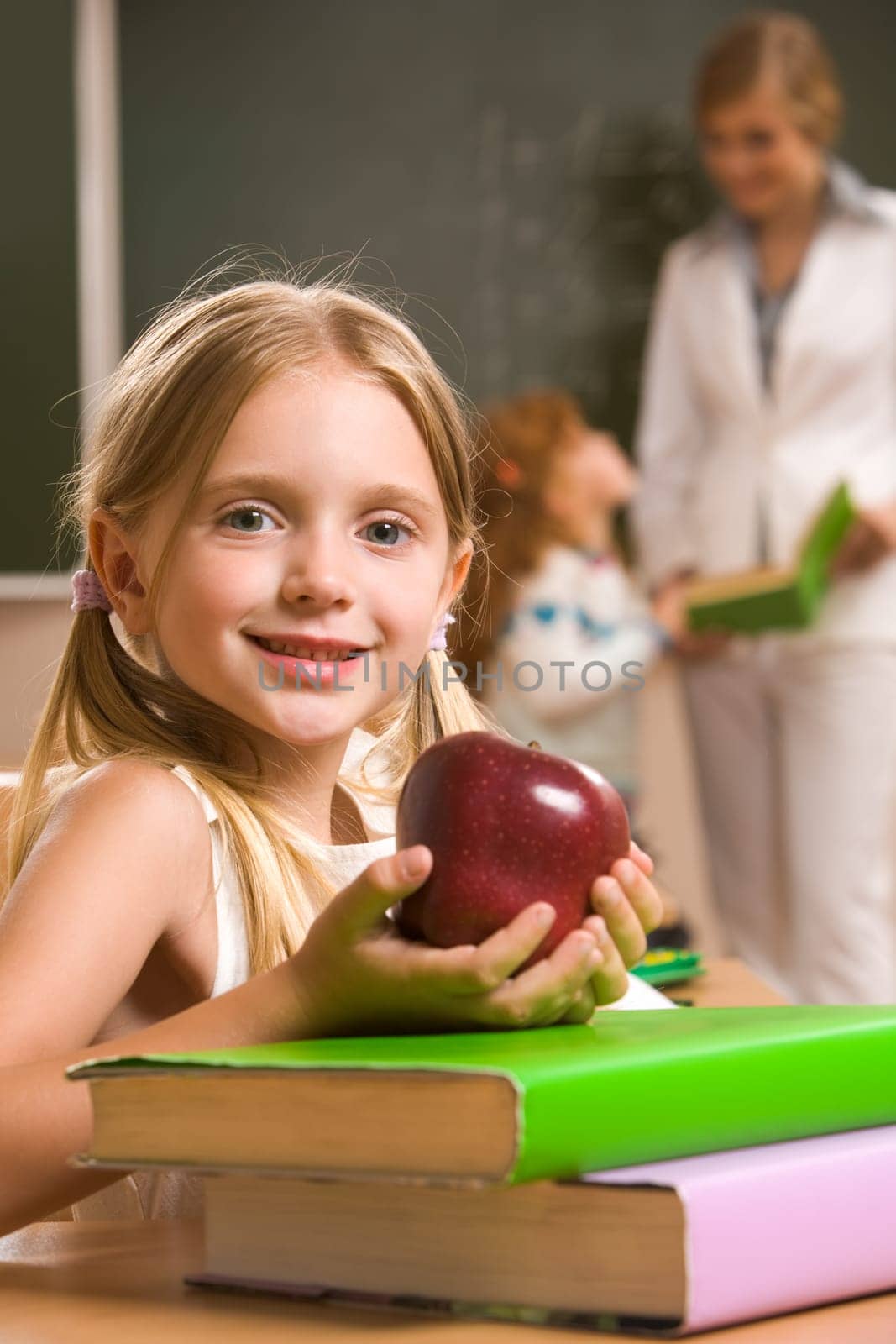 Portrait of happy schoolgirl and apple in her hands sitting at the table with books