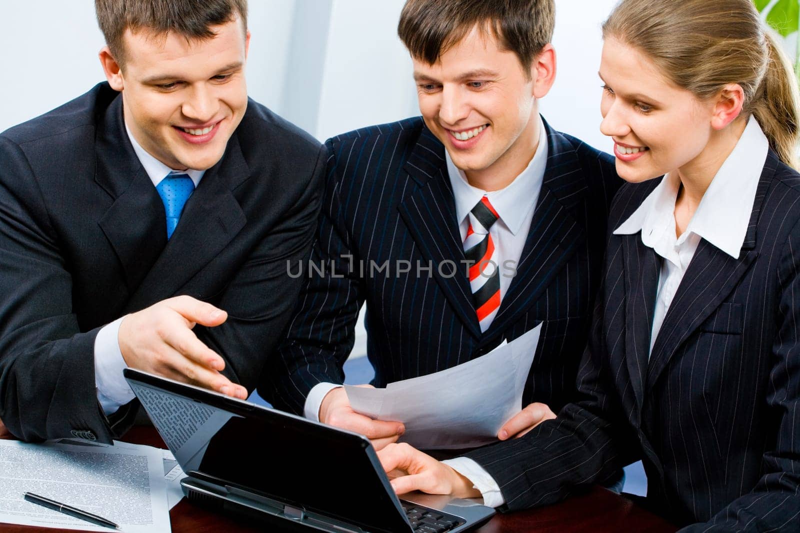 Portrait of three young specialists looking at monitor of laptop