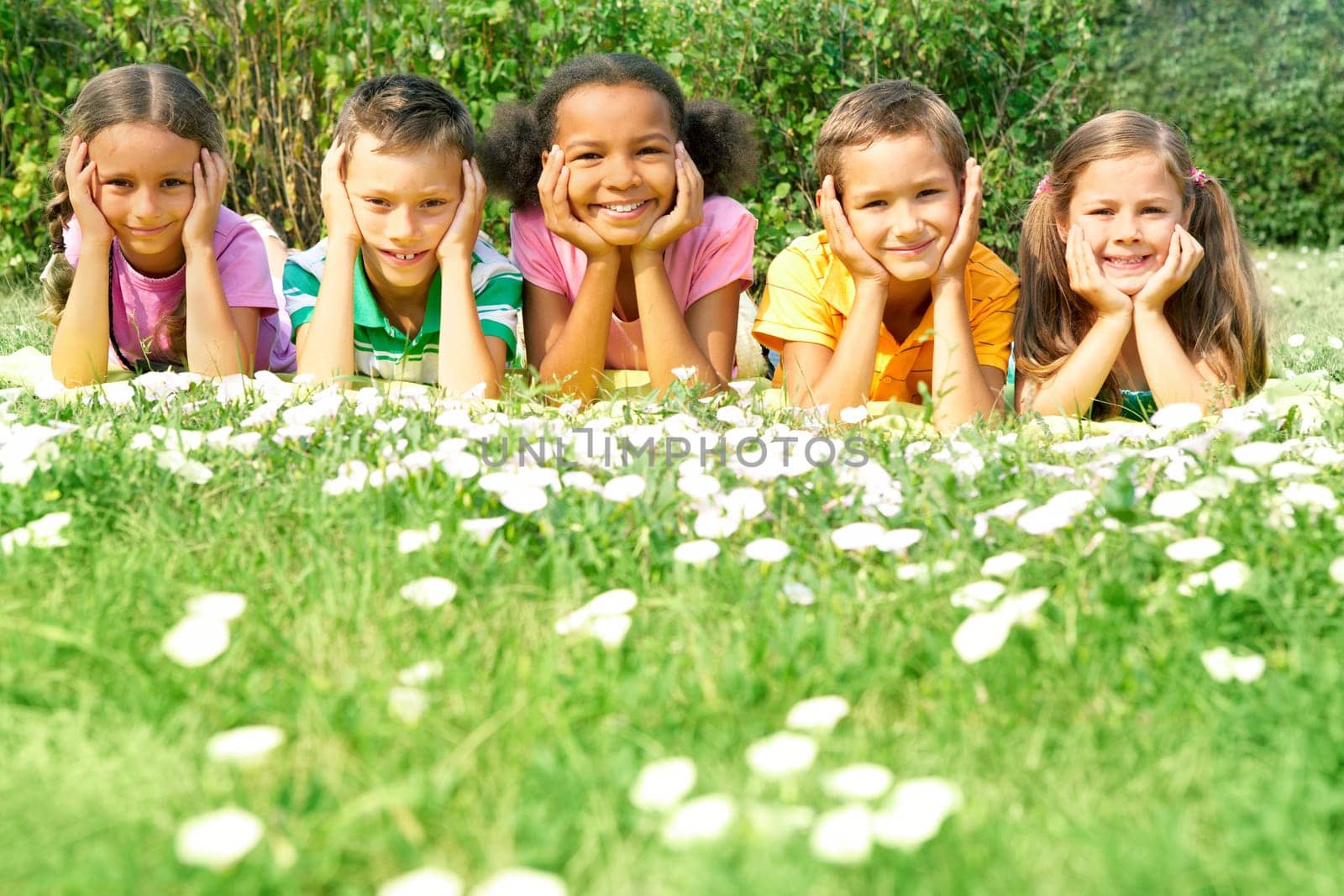 Portrait of cute kids lying on green grass and looking at camera