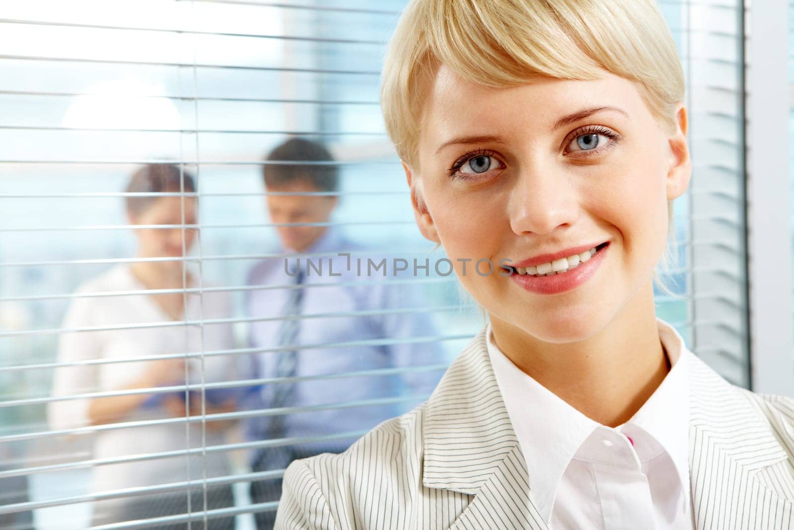 Female leader looking at camera with two partners interacting in office behind