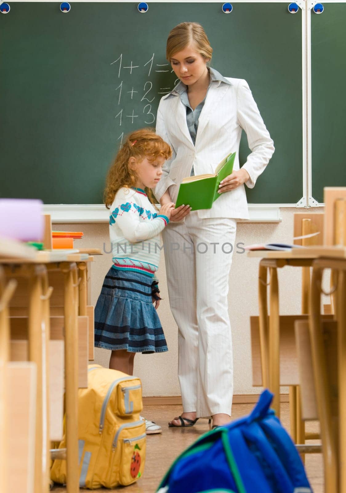 Photo of schoolgirl and teacher reading book together in the classroom