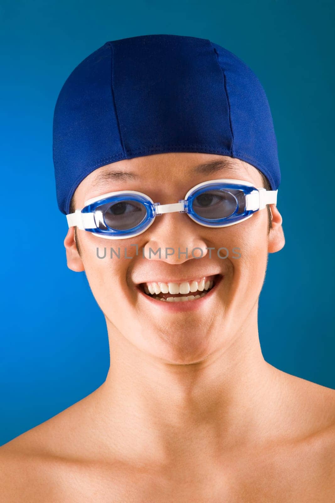 Portrait of happy sportsman in swimming cap and goggles over blue background
