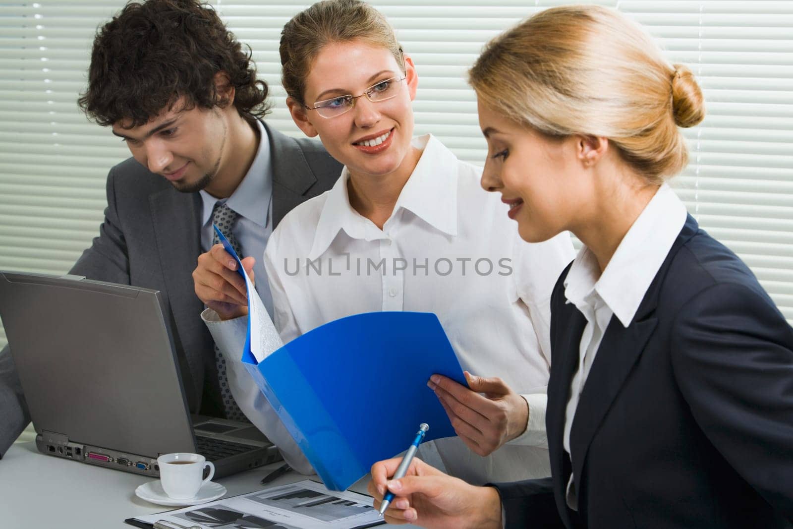 Group of three young business people gathered together discussing an interesting idea in the office