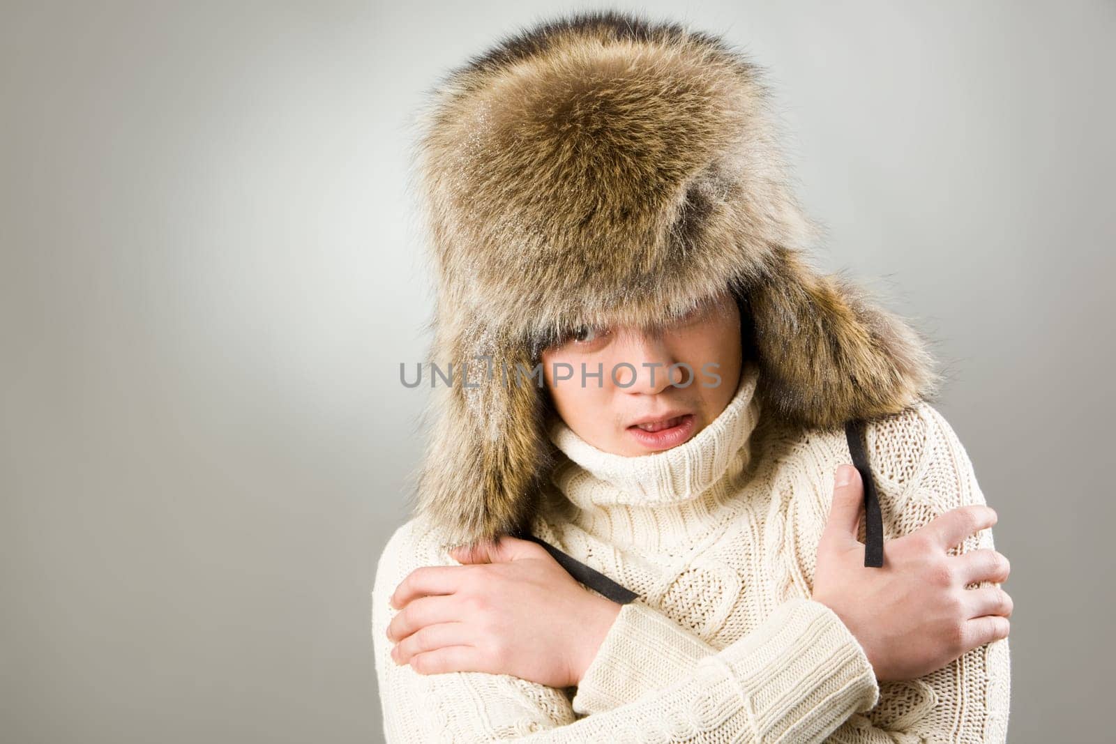 Portrait of man in warm fur hat and knitted sweater showing coldness
