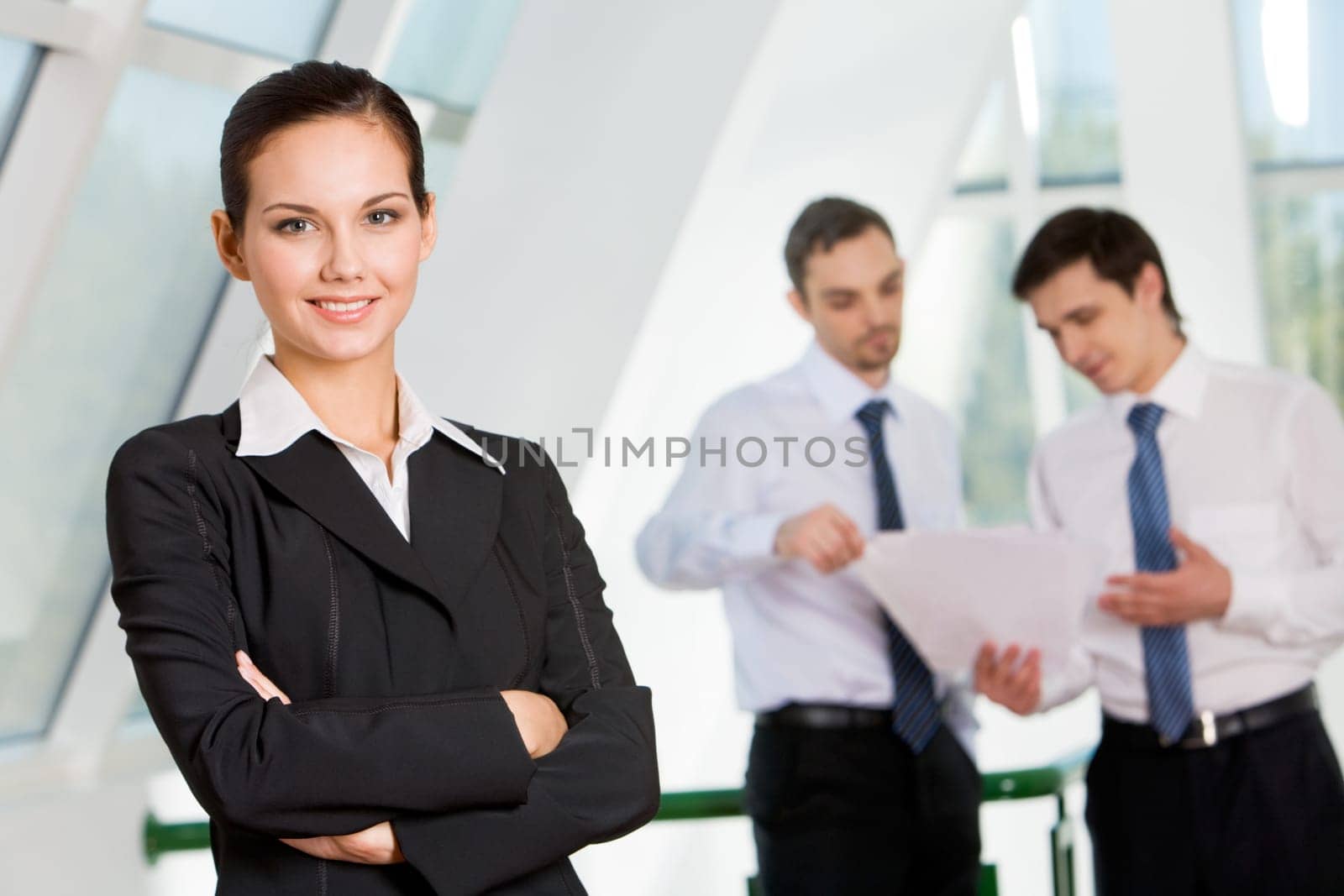 Portrait of attractive business lady looking at camera with smile on background of interacting men