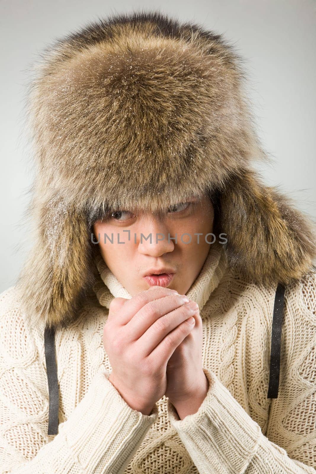Portrait of cold man in fur hat and knitted sweater warming up his hands