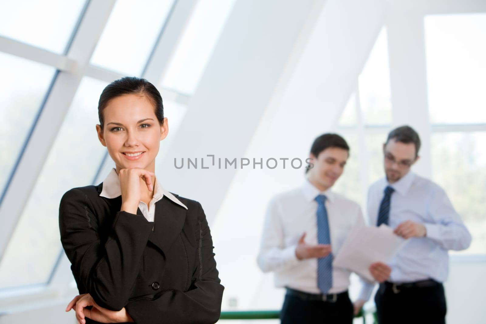 Portrait of attractive business lady looking at camera with smile with men discussing ideas at background