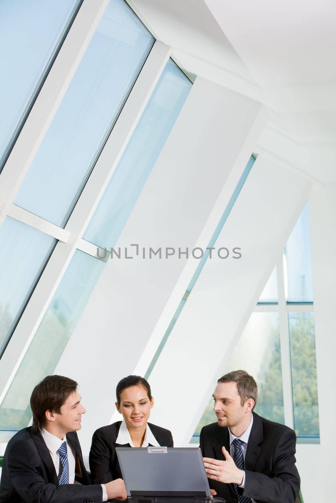 Portrait of three confident colleagues speaking about new project with laptop near by