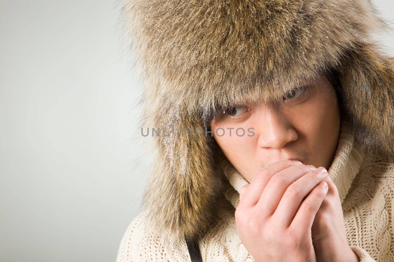 Portrait of cold man in fur hat and knitted sweater warming up his hands