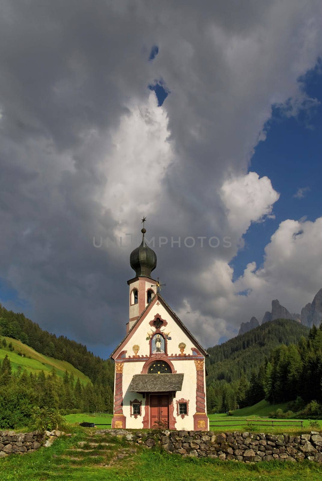 Small Church of St. John in Ranui with Odle Mountains and a dramatic cloudy sky,Funes Valley,Dolomites,Suedtitol,Italy