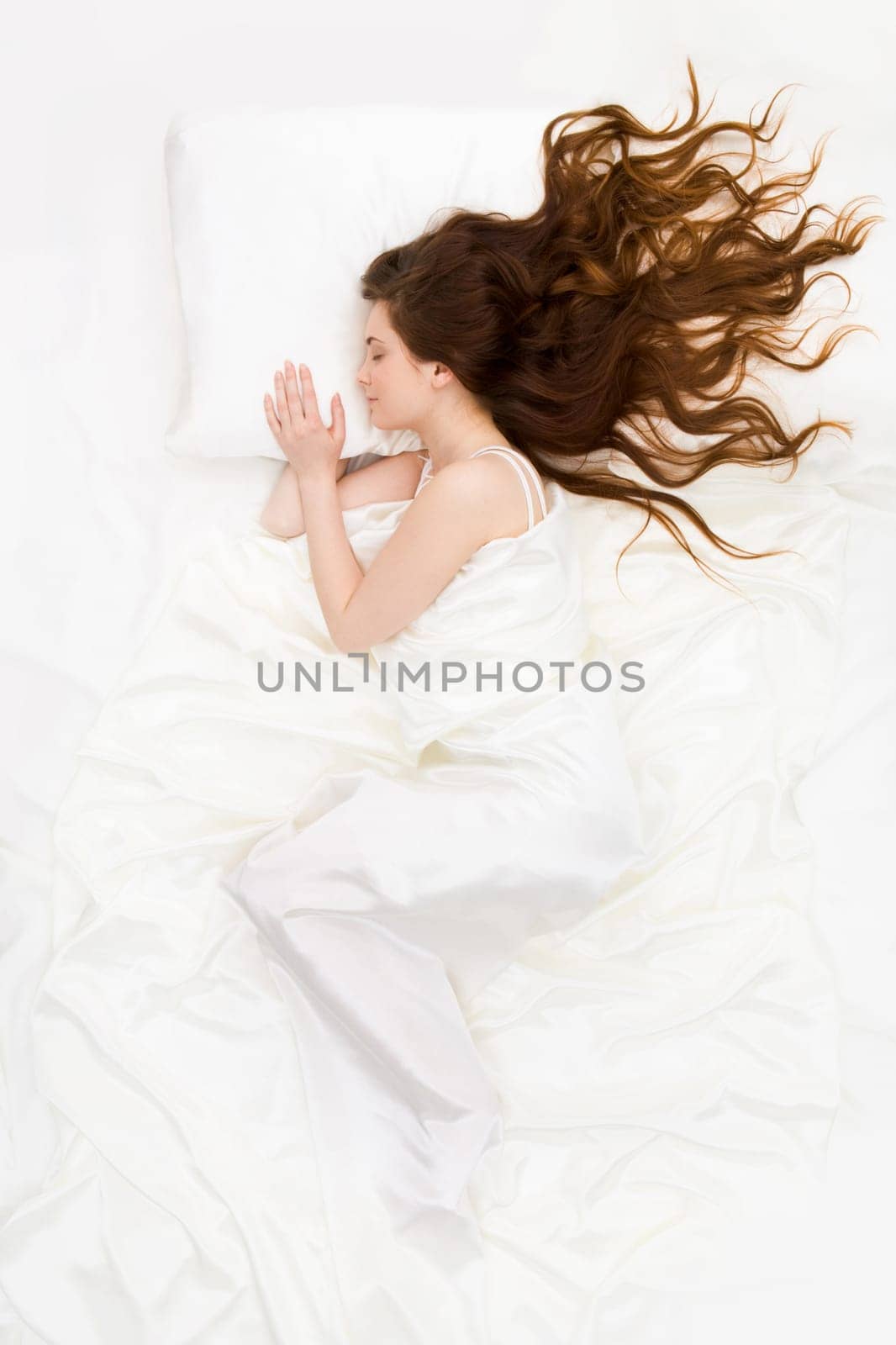 Above view of sleeping woman under white satin sheet