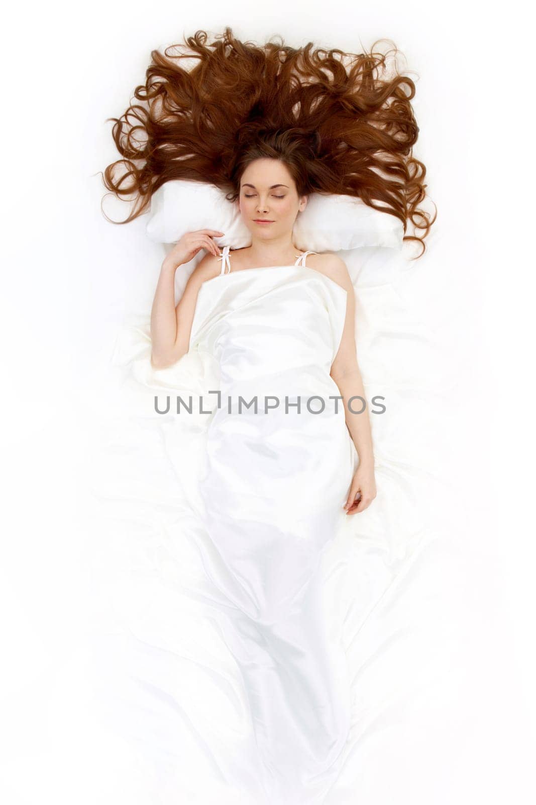 Above view of resting female under linen sheet with her long hair spread on pillow