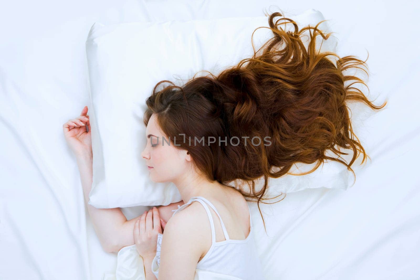 Photo of pretty long-haired woman sleeping peacefully in white bed