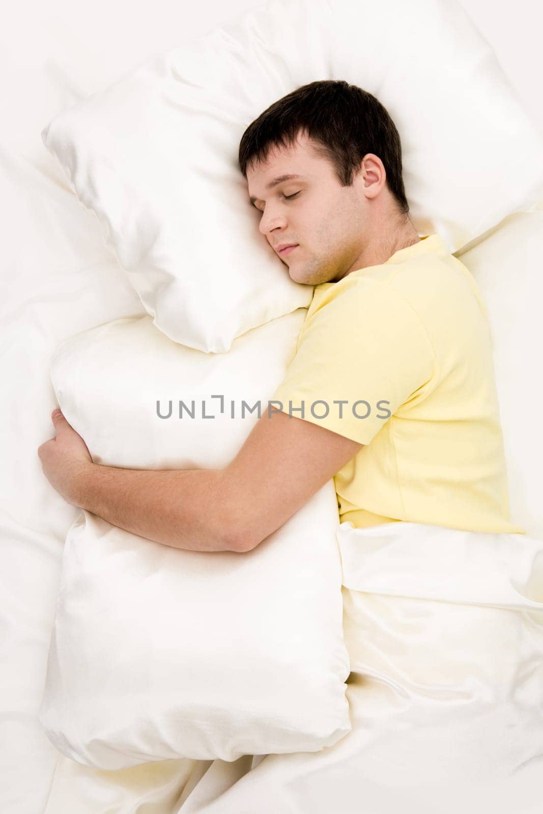 Photo of handsome man sleeping and holding soft white pillow