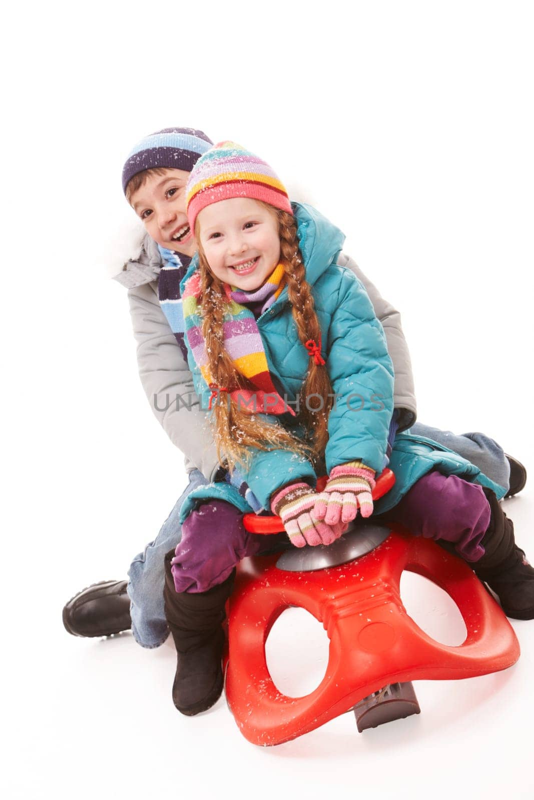 Happy siblings looking at camera while sitting on sledge