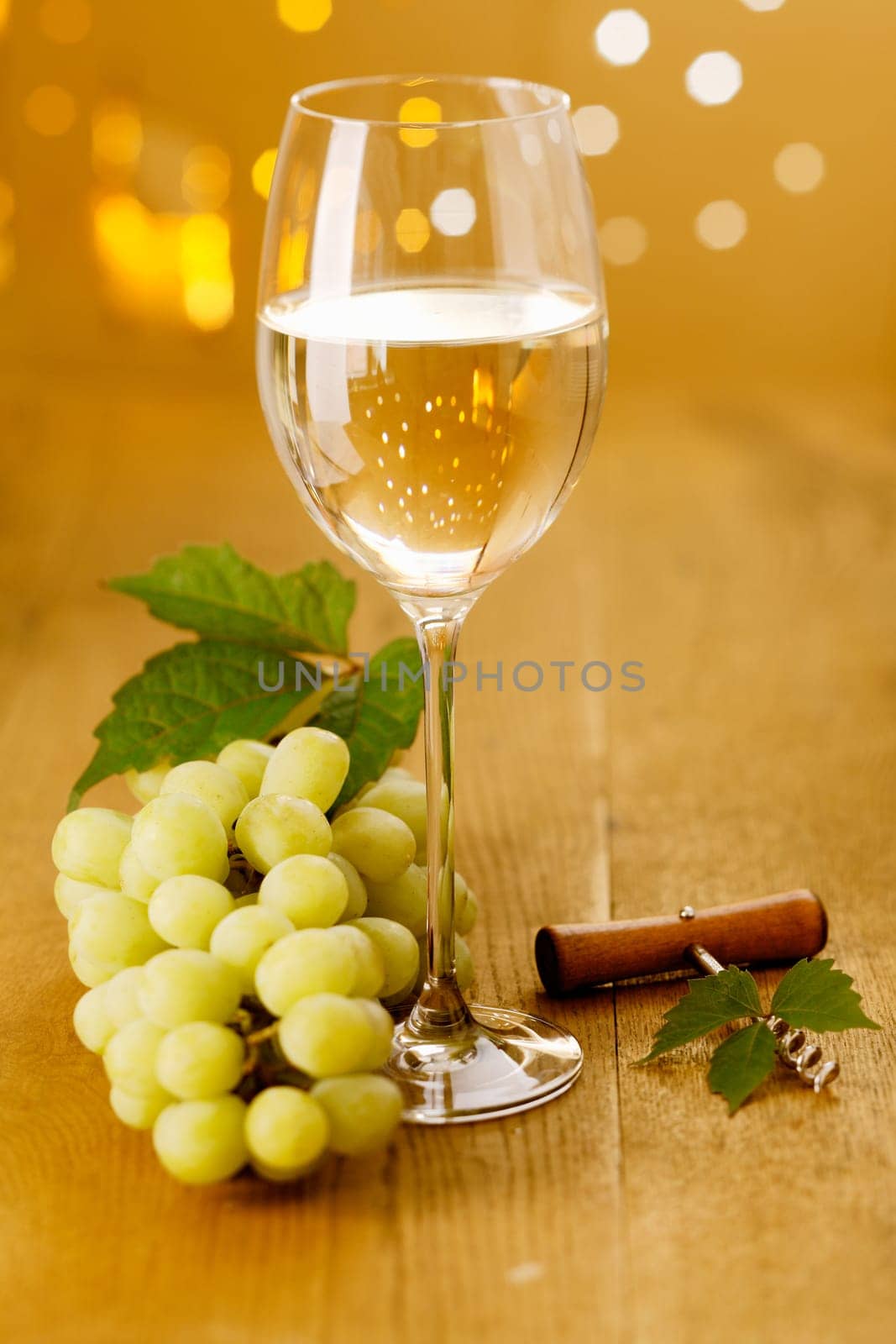 Glass of white wine and grapes with a corkscrew against a festive bokeh of party lights