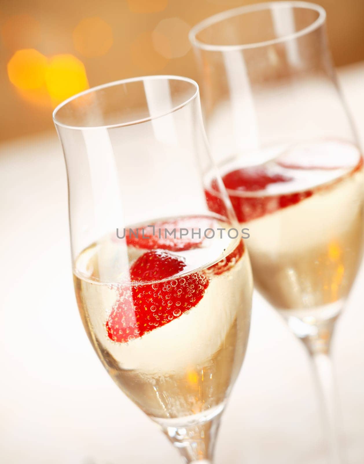 Closeup of stylish champagne flutes filled with chilled bubbly and a floating strawberry for celebrating a romantic evening together