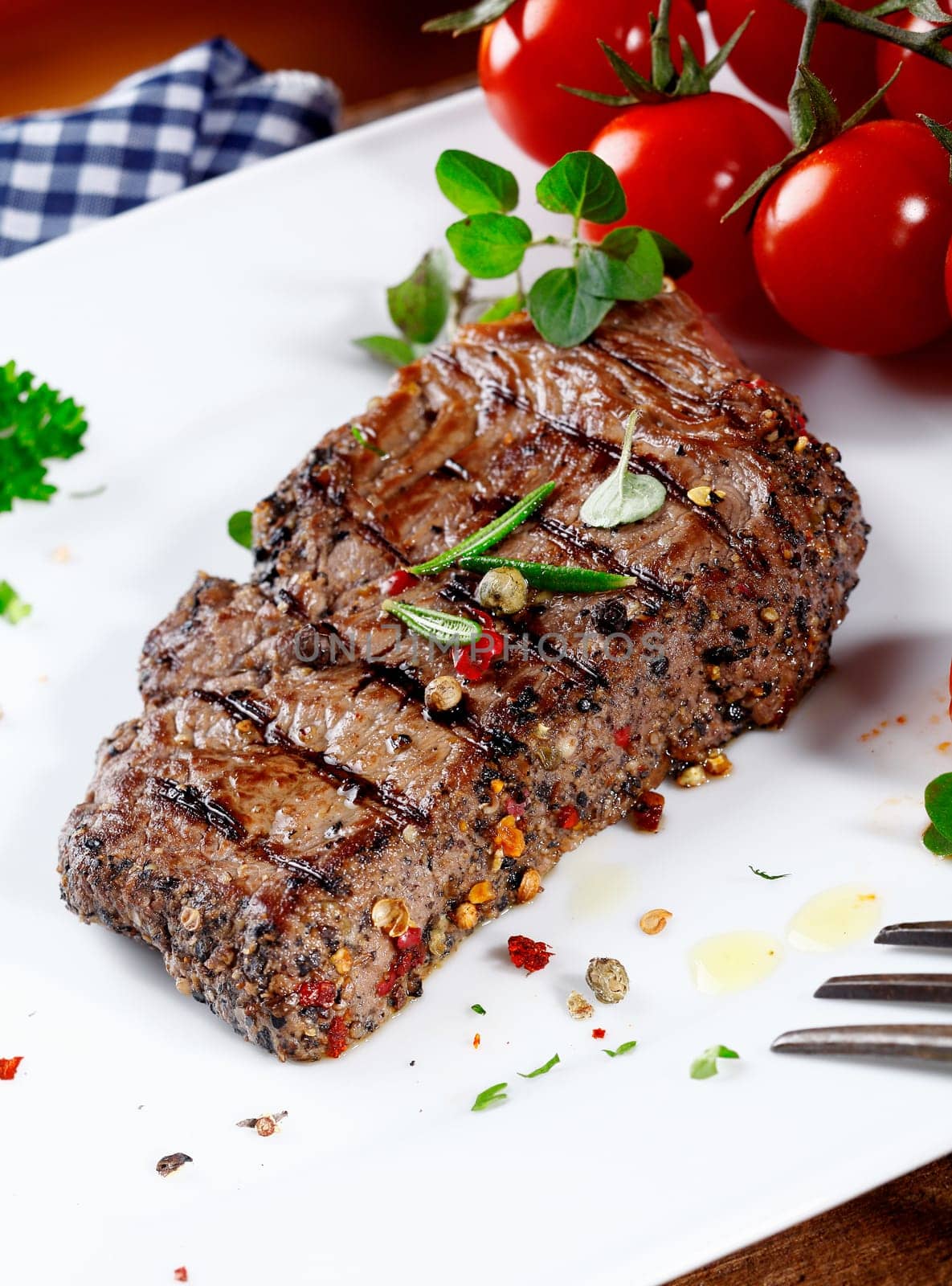 Thick portion of succulent tender peppered steak grilled to perfection and served on a plate with fresh herbs and tomatoes