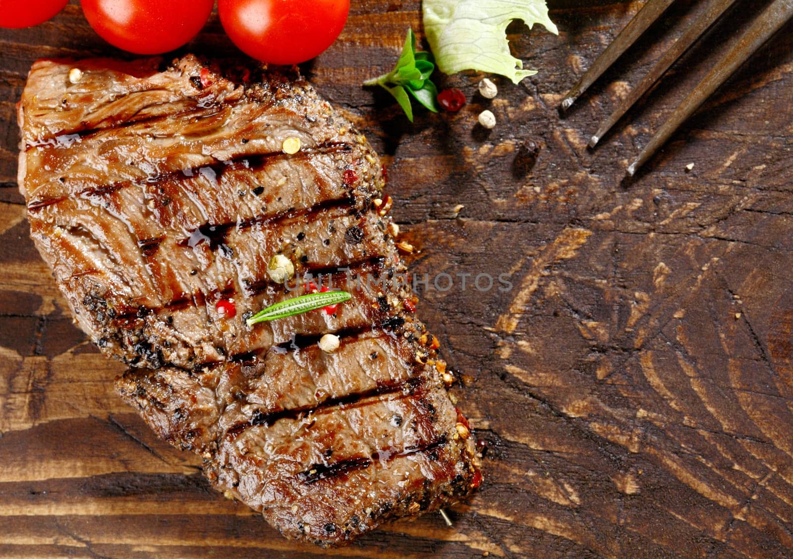Overhead view of a portion of juicy grilled beef steak with peppercorns on a textured wooden surface