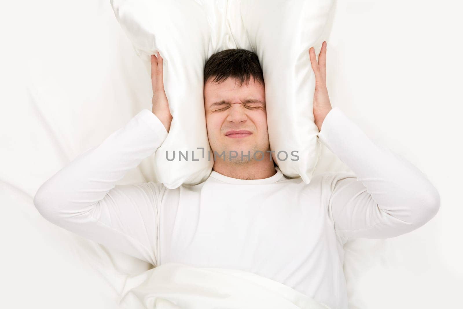 Image of man suffering from insomnia and shutting ears with cushion