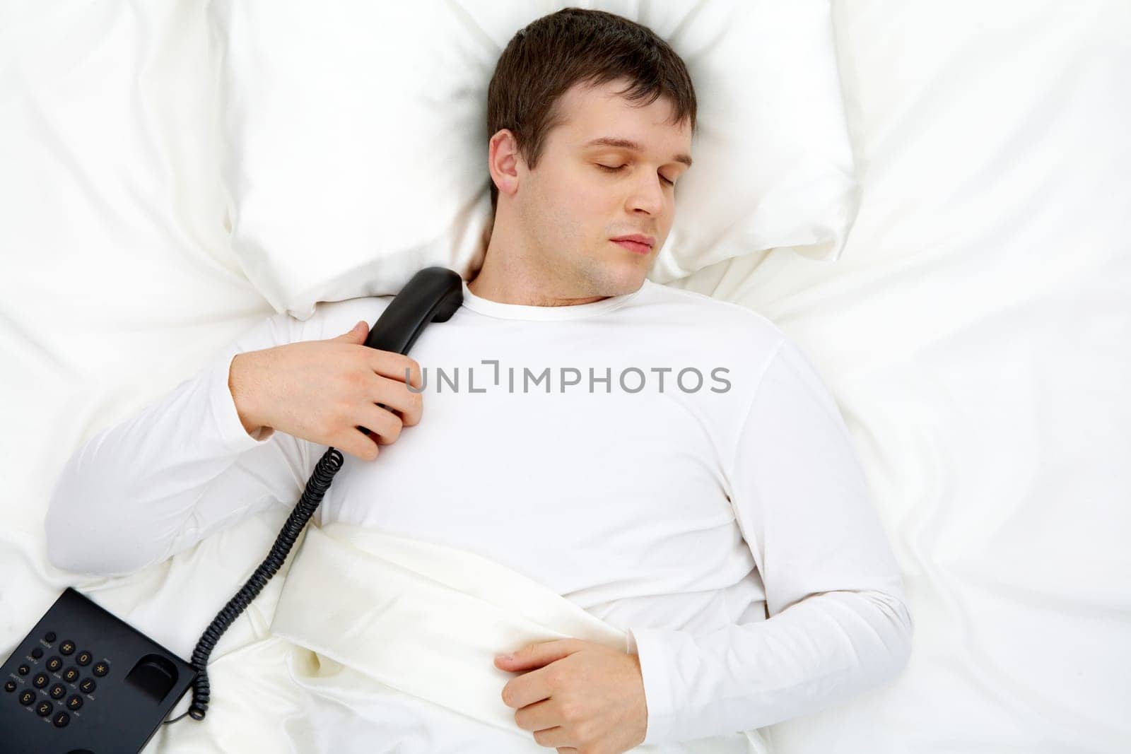 Image of handsome man having rest in bed with telephone near by