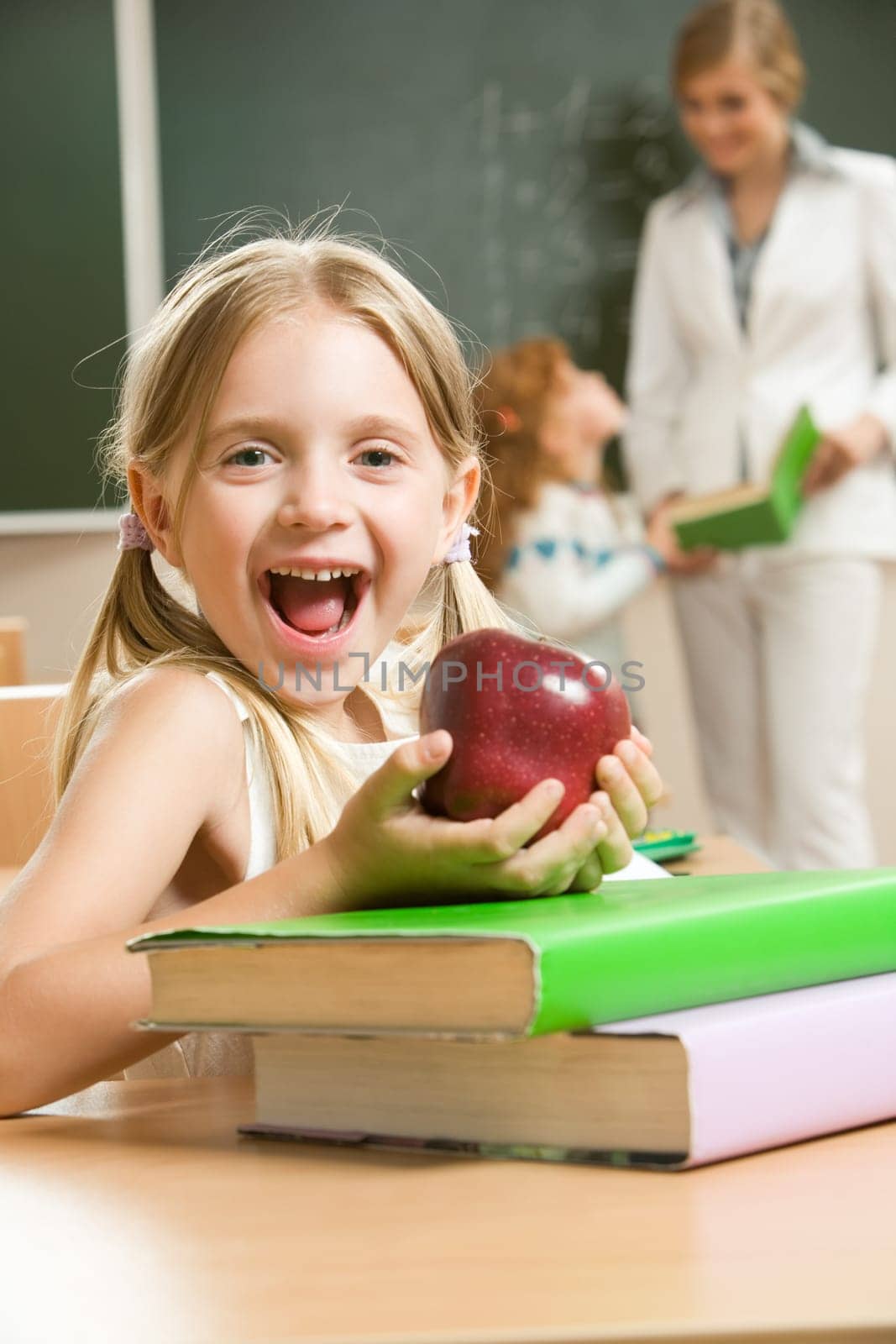 Portrait of happy schoolgirl and apple in her hands sitting at the table with books