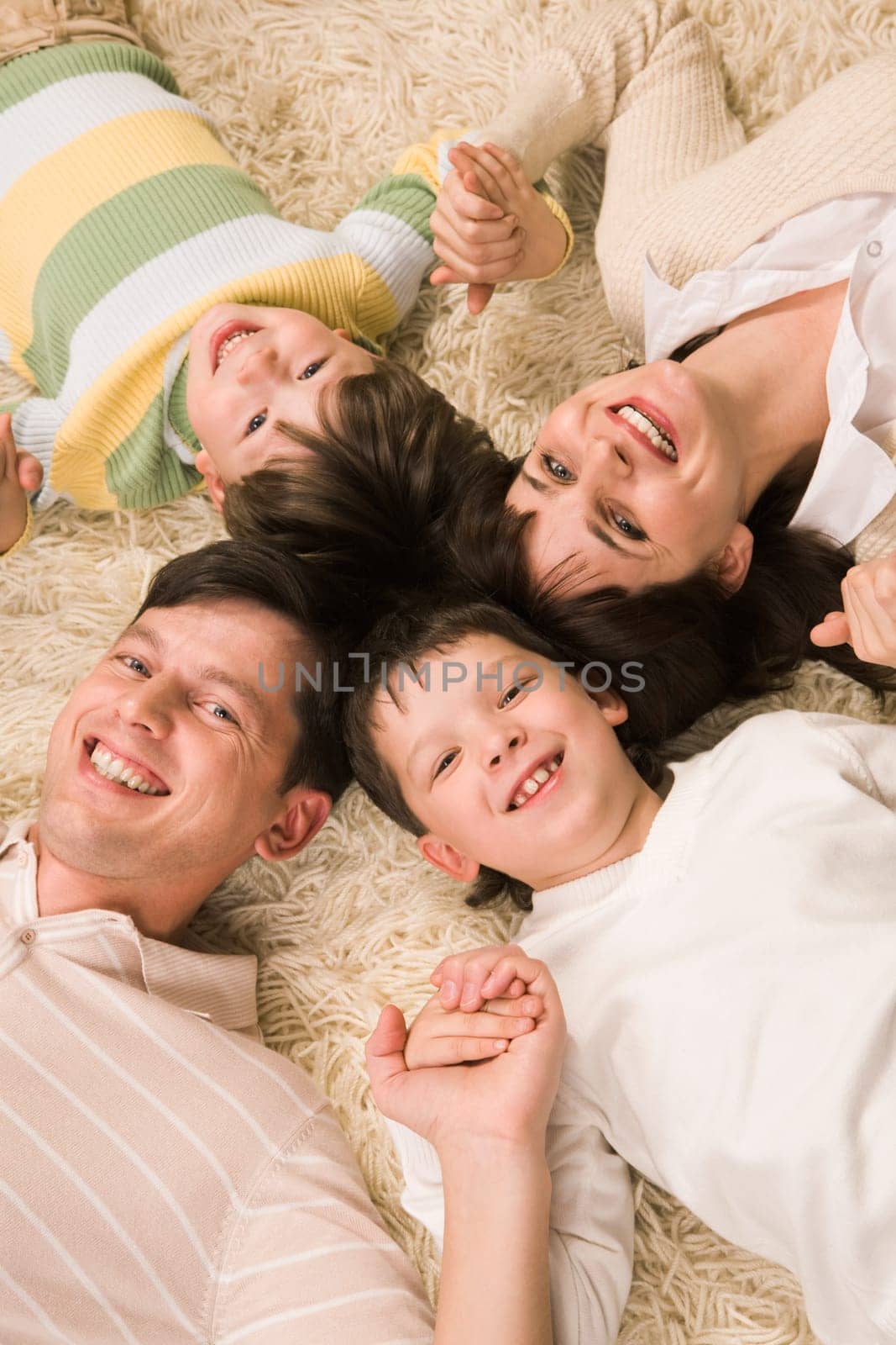Above view of cheerful couple with their two sons holding by hands and smiling at camera