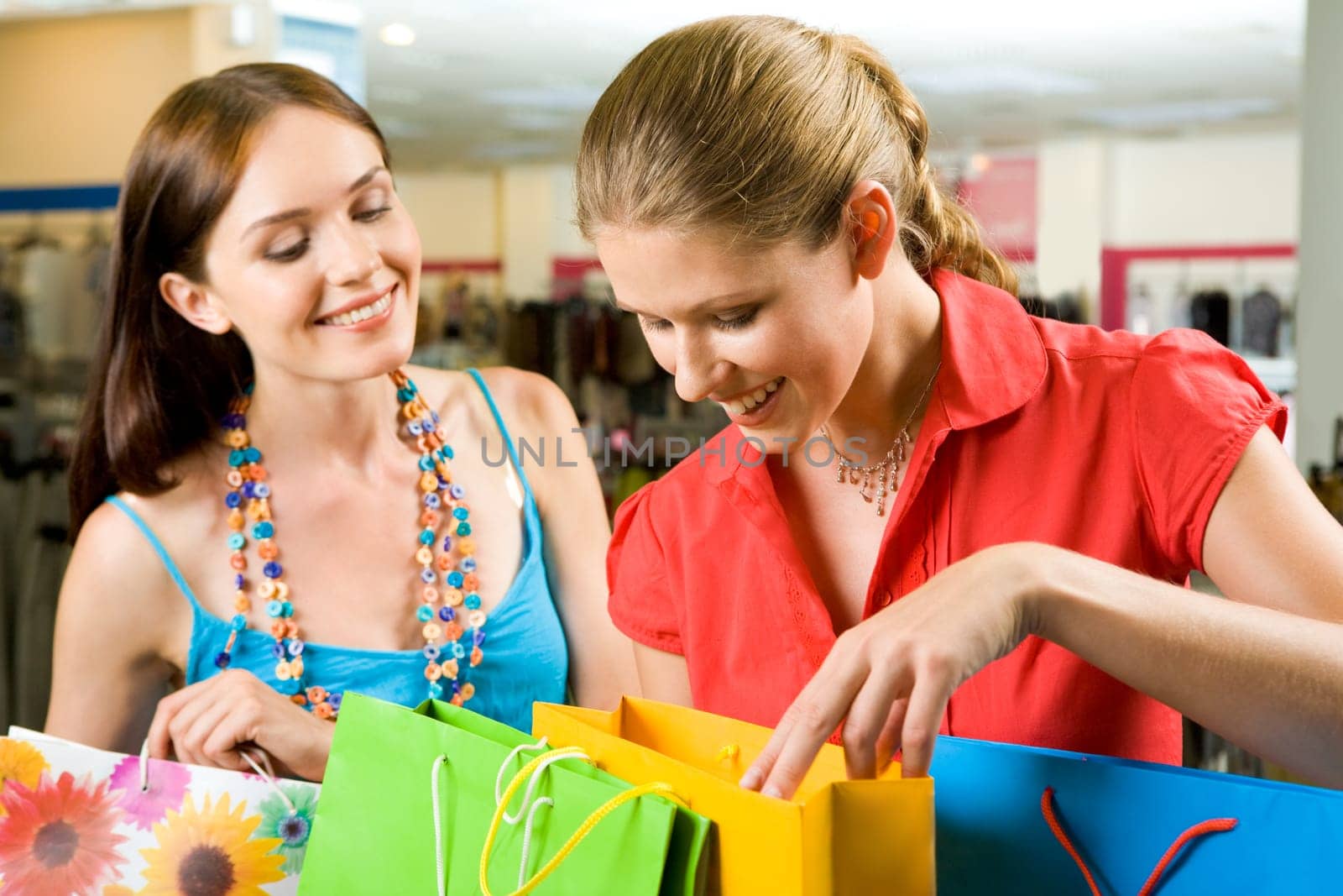 Photo of two friends looking through their shoppings with smiles in the mall