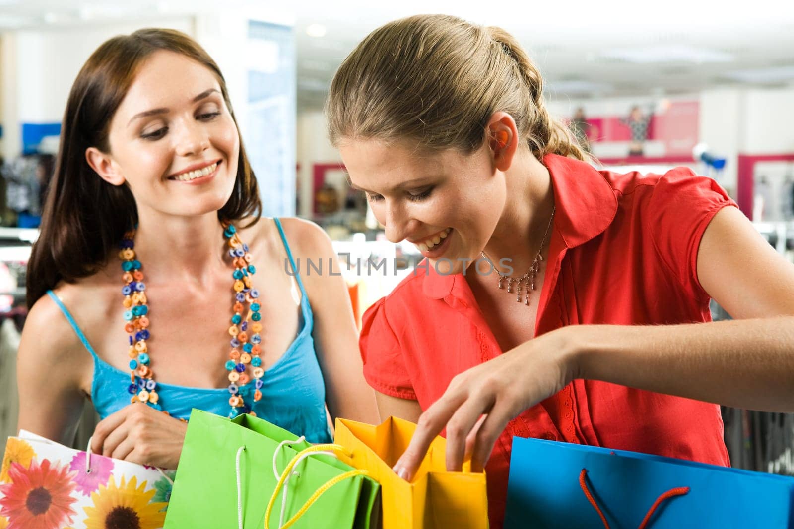 Photo of two friends looking through their shoppings with smiles in the mall