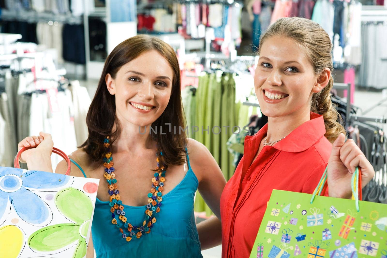 Portrait of cheerful girls carrying shopping bags and looking at camera happily in the mall
