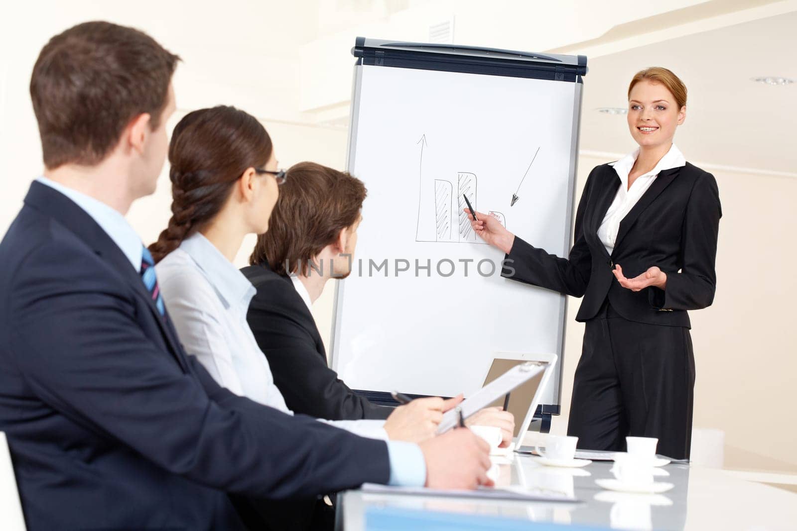 Smart and confident employee pointing at whiteboard while presenting her ideas to business partners
