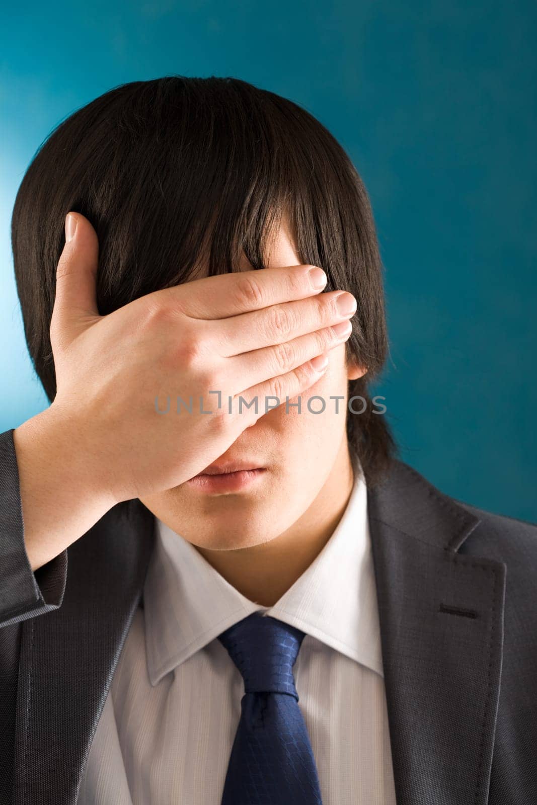 Portrait of young businessman hiding his face by hand