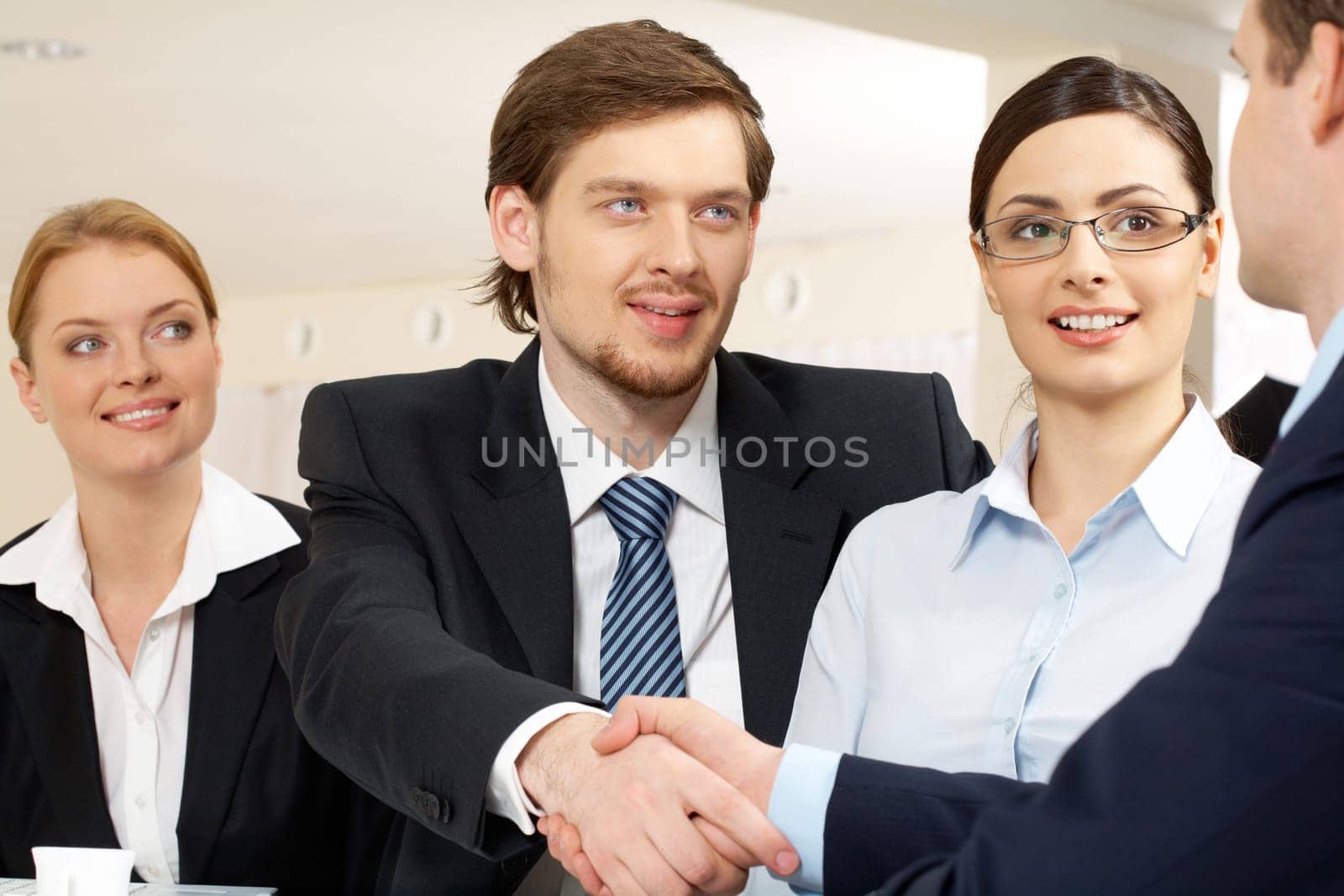 Photo of successful business partners handshaking after striking deal with pretty employees near by