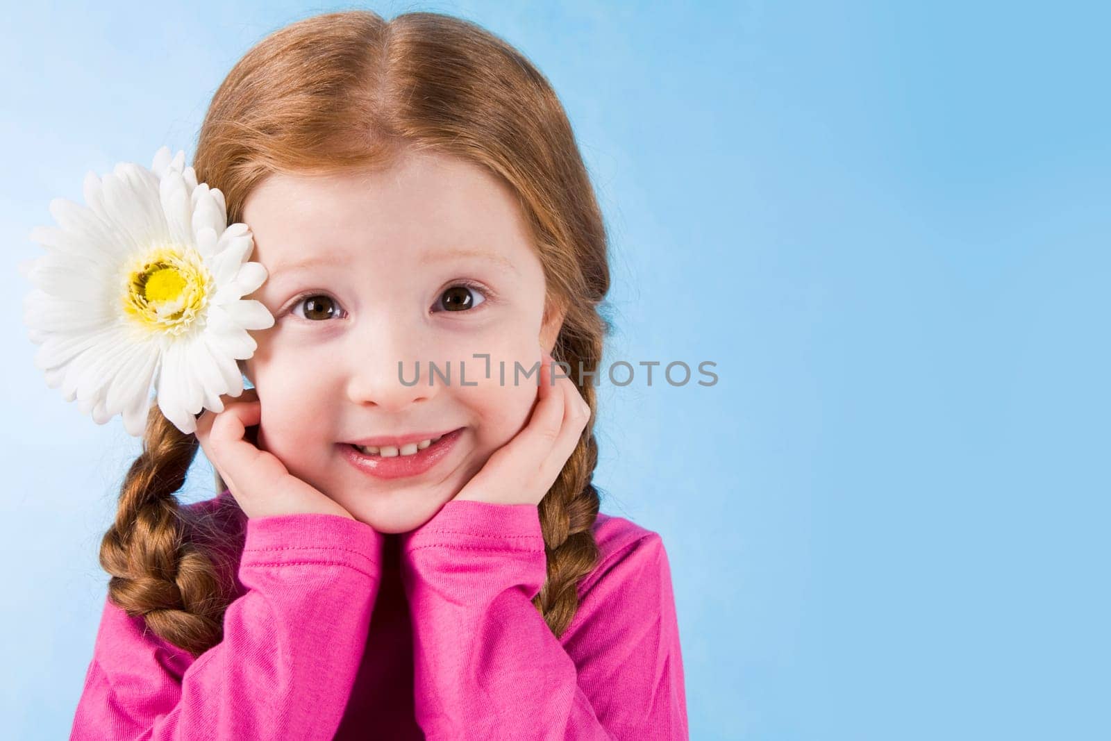 Portrait of charming girl with flower in hair touching her face over blue background