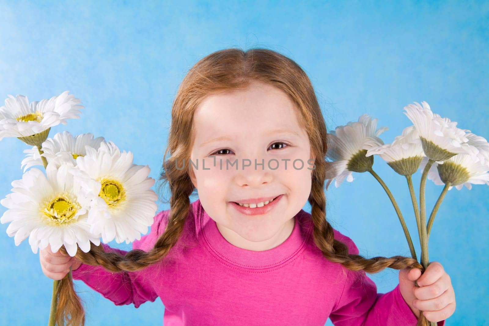 Portrait of joyful girl holding her pigtails and flowers in both hands