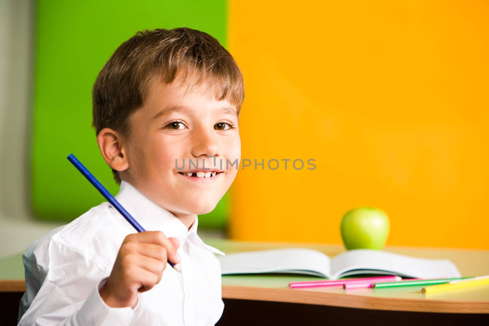 Portrait of handsome schoolboy holding pencil in hand and looking at camera