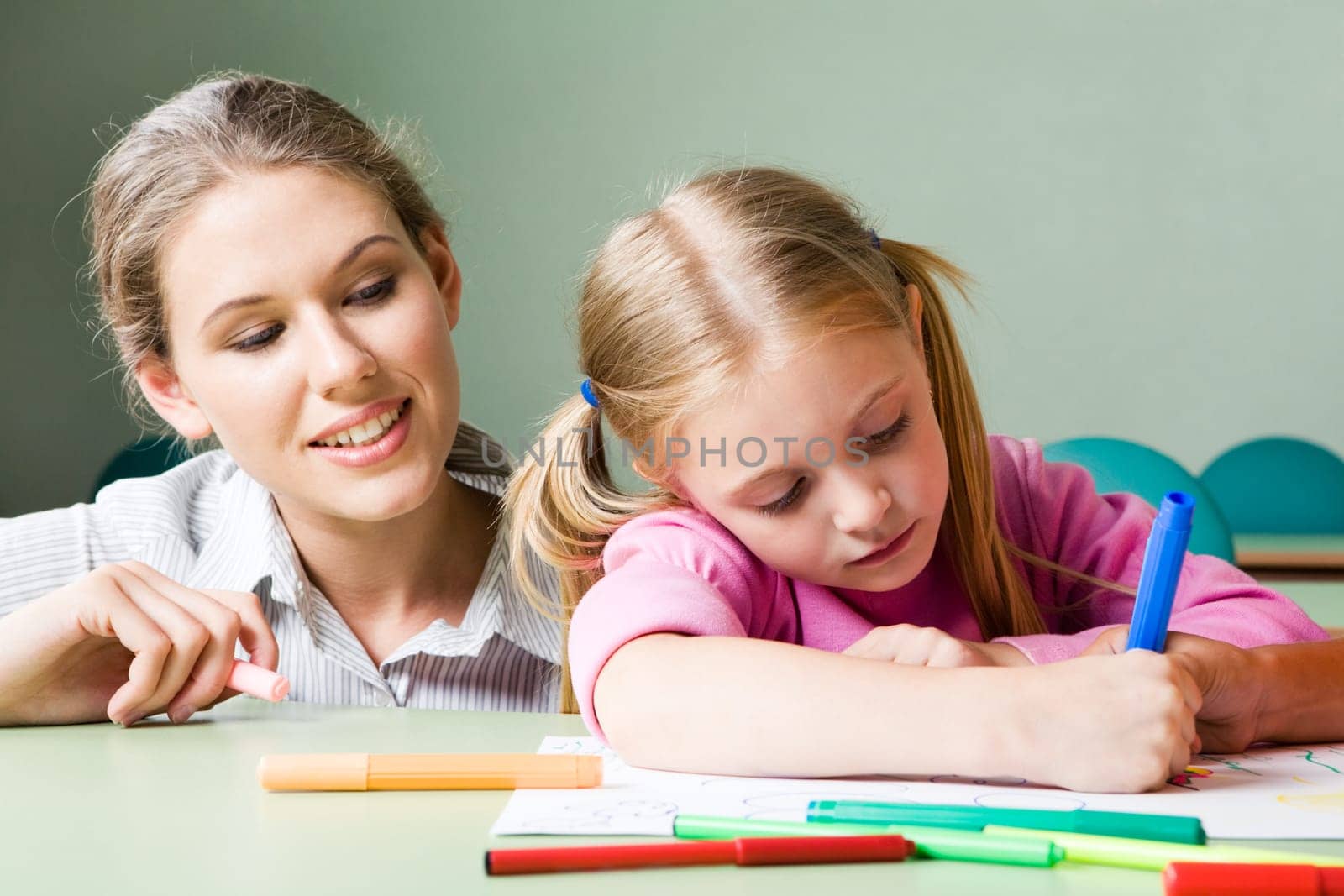 Portrait of diligent girl drawing something under tending of her teacher