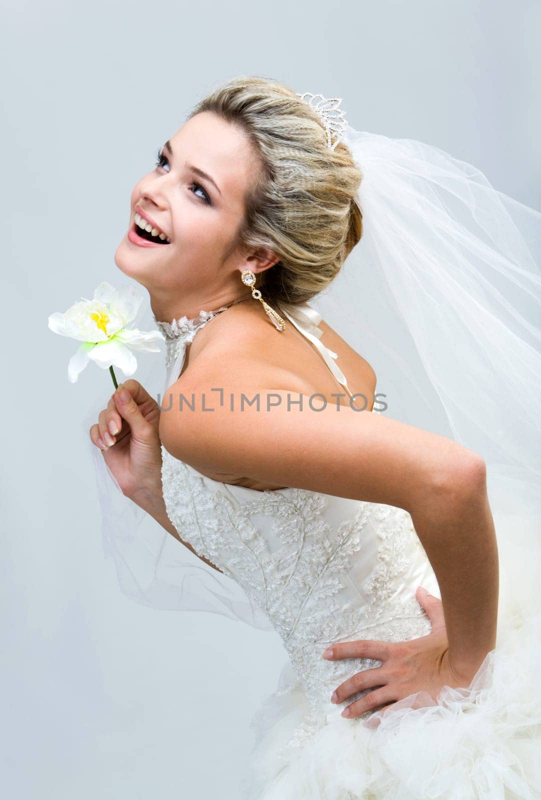 Portrait of joyful bride holding flower in hand and laughing while looking upwards