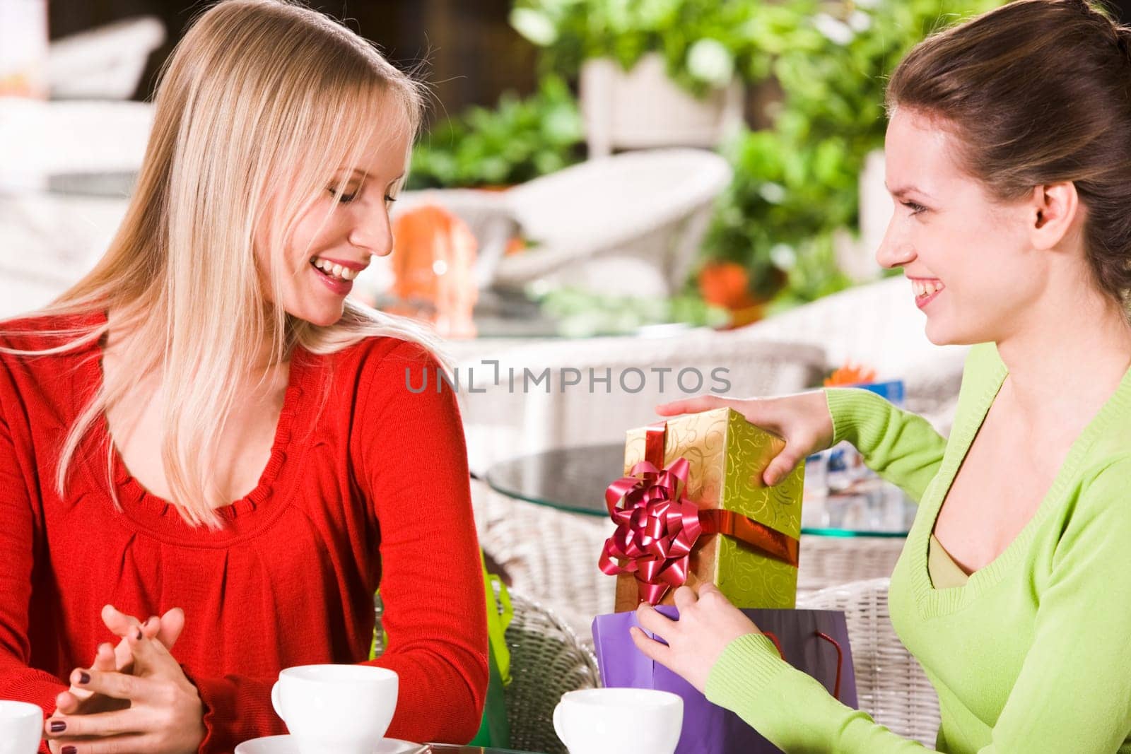 Photo of happy girl putting giftbox into paperbag after showing it to her friend
