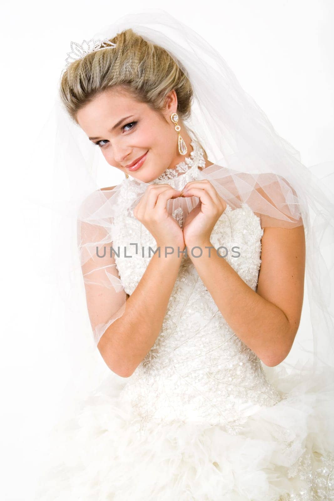 Portrait of bride wearing snow-white beautiful dress and making shape of heart with her hands while looking at camera