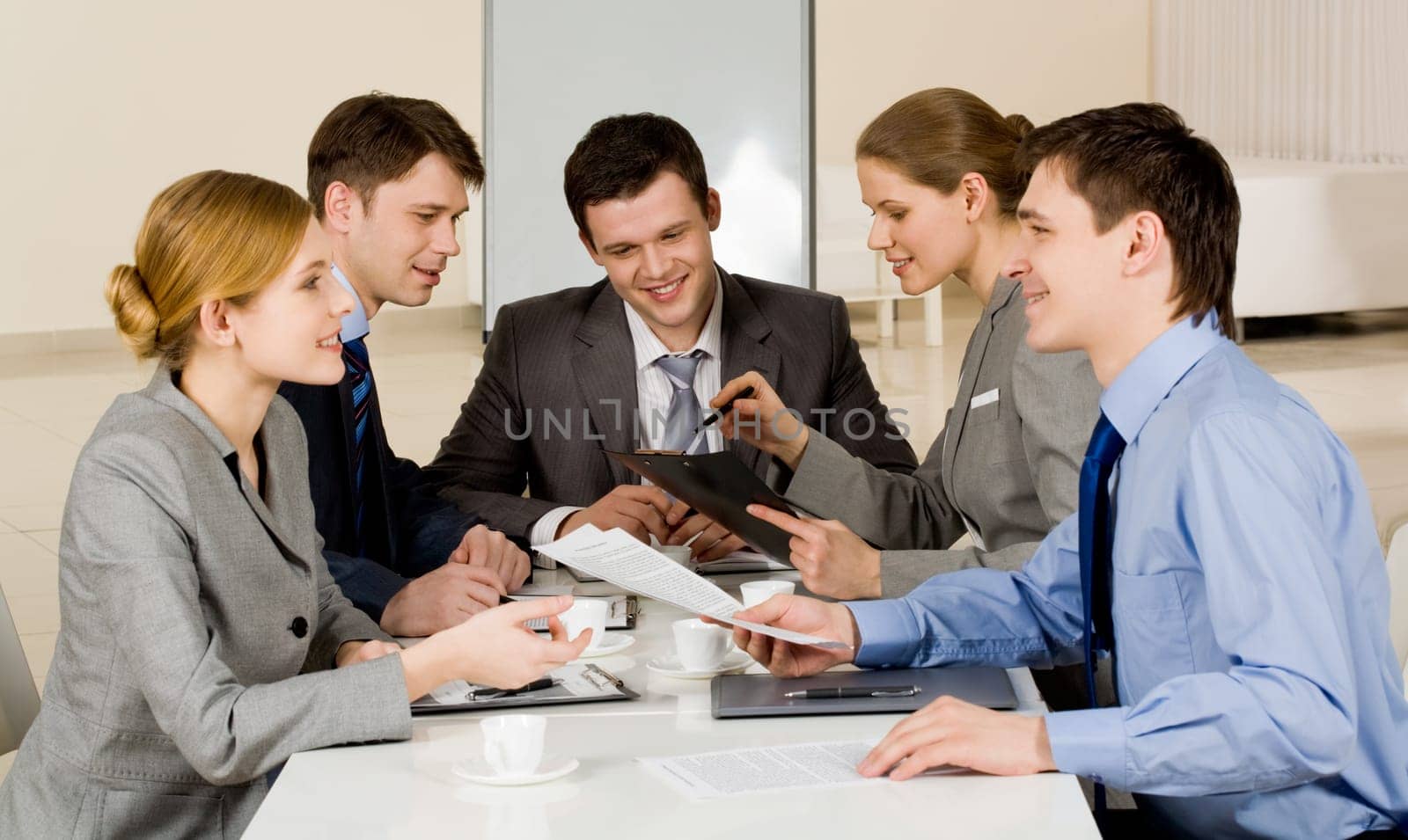 Portrait of friendly colleagues looking at each other while confident woman sharing her idea with co-workers on background