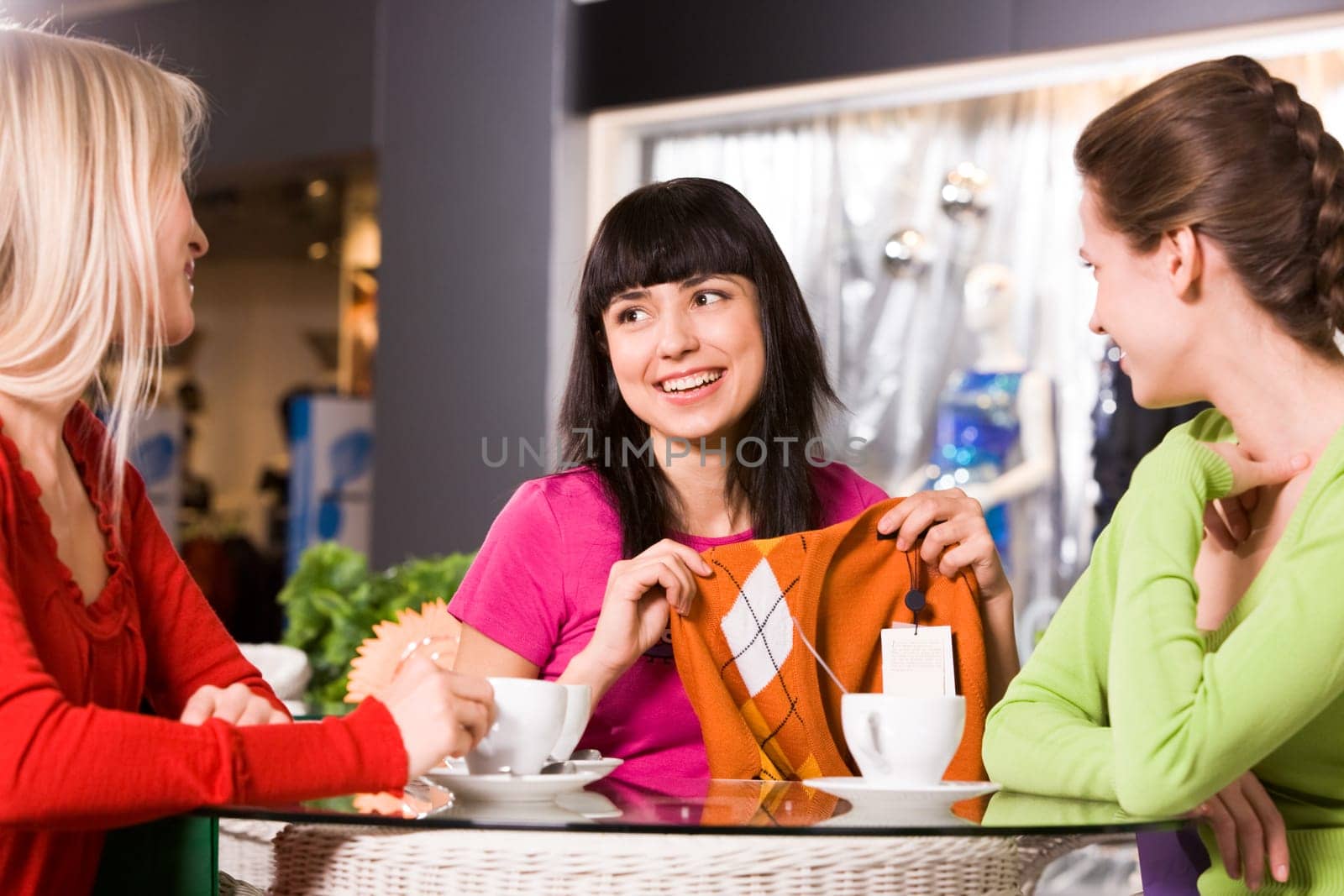 Photo of happy girl showing fashionable pullover to her friends in cafe