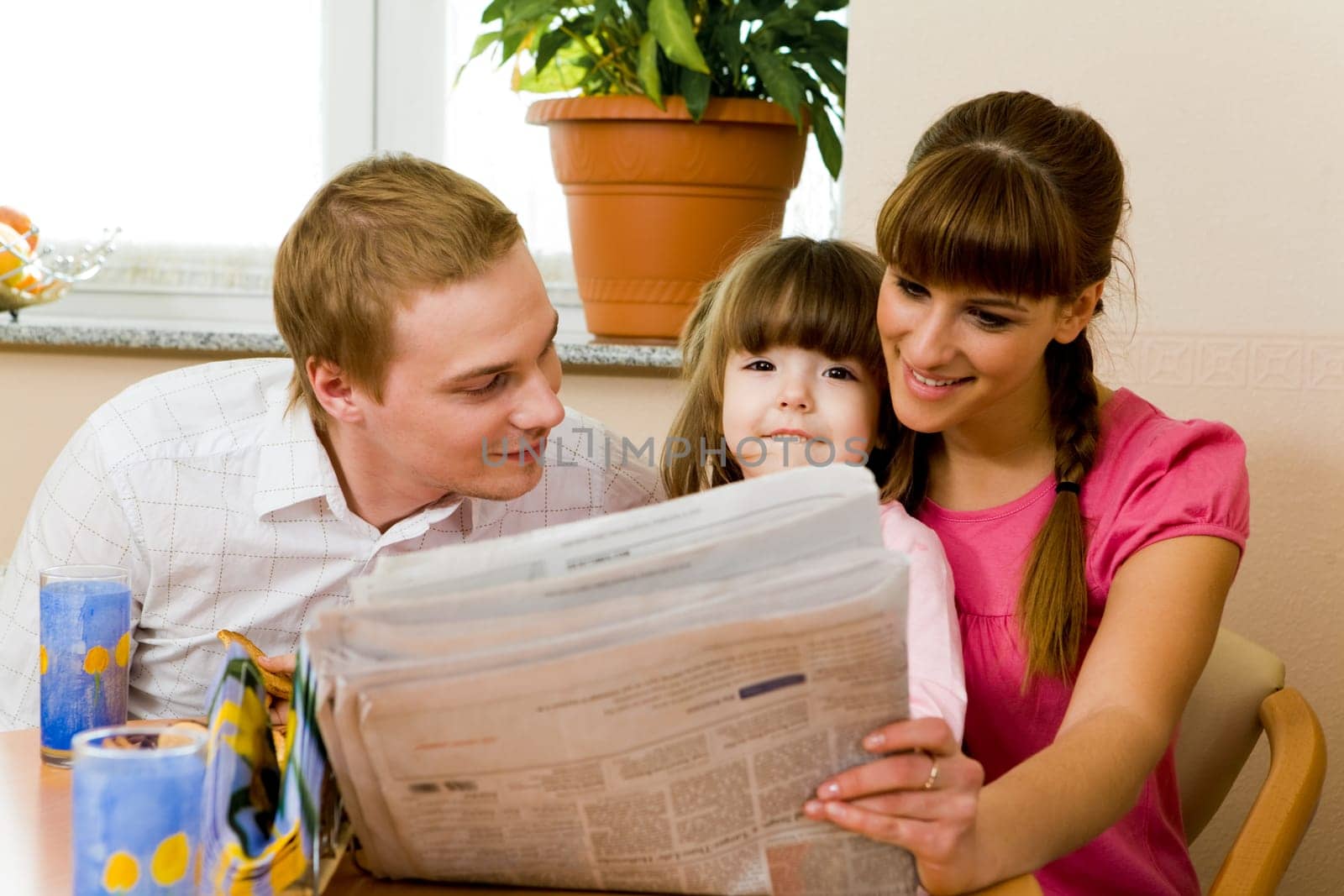 Photo of affectionate family reading newspaper in females hands while her husband looking at cute girl