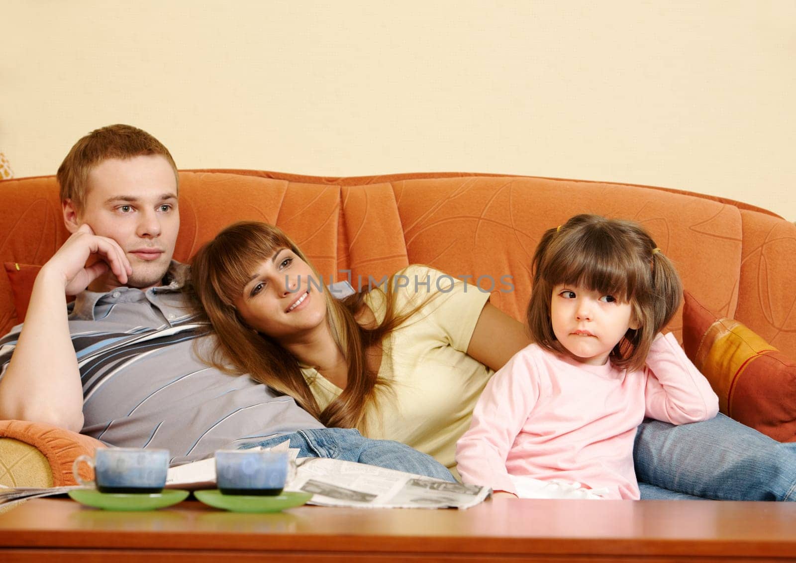 Happy couple and their daughter relaxing on sofa and watching TV